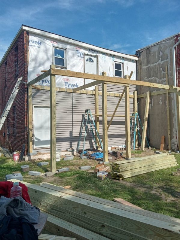 New framing built against the back wall of a house that is wrapped and ready for siding